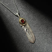 Handcrafted sterling silver feather pendant necklace with brass accent and a red gemstone centerpiece.