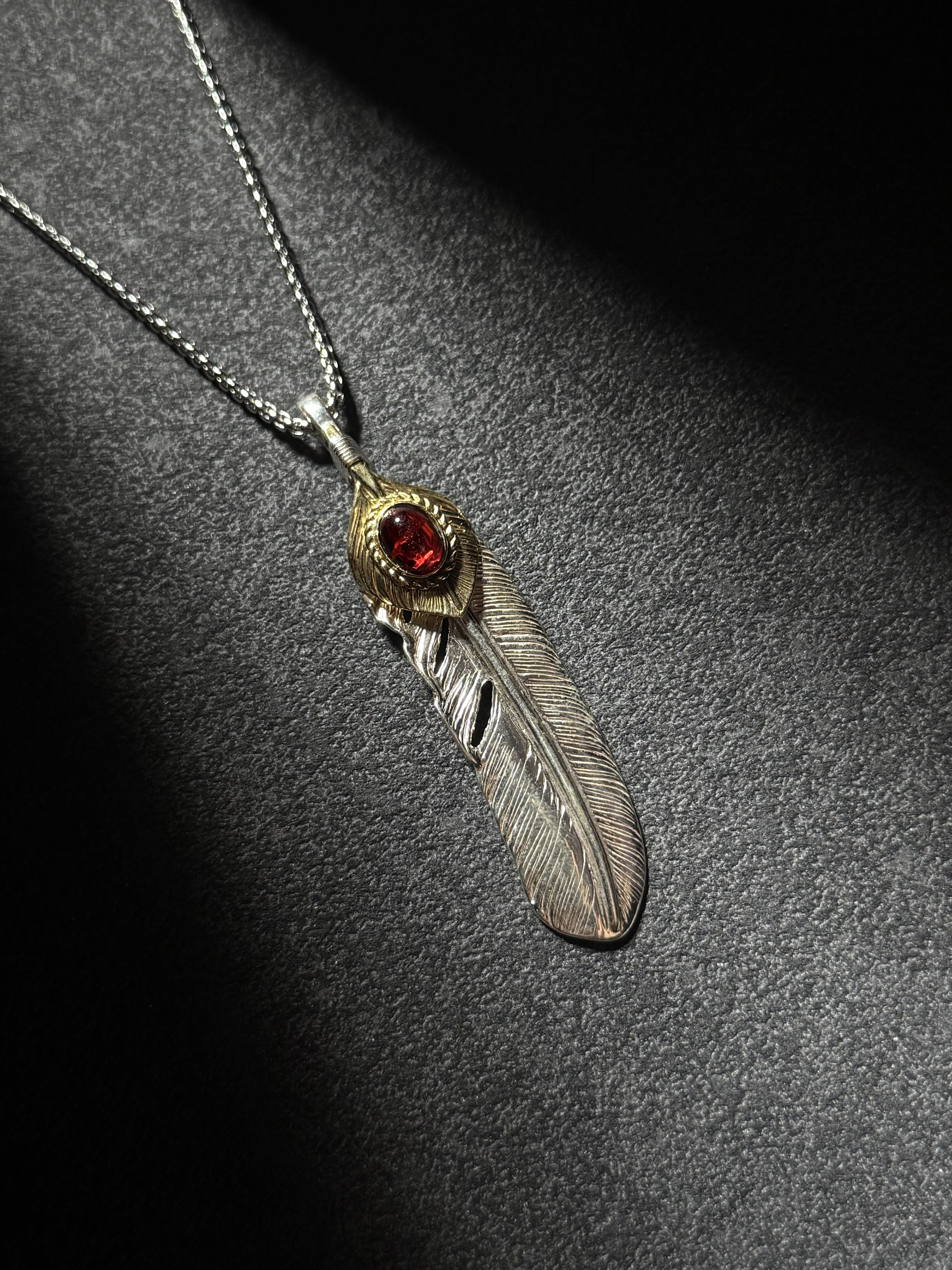 Handcrafted sterling silver feather pendant necklace with brass accent and a red gemstone centerpiece.