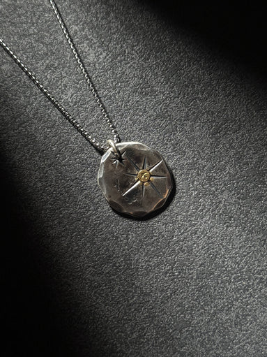 North Star sterling silver pendant necklace with brass center on dark textured background